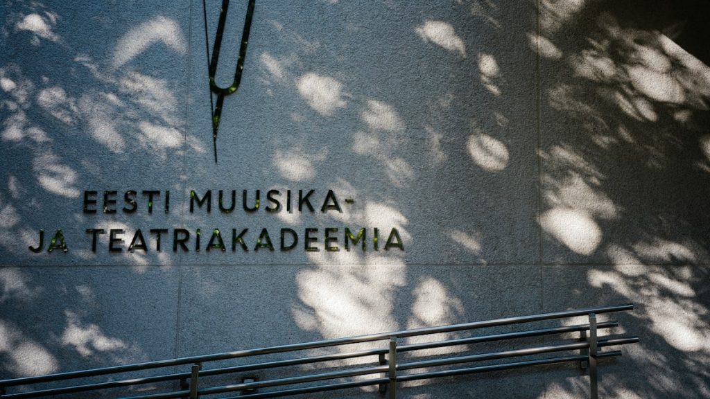A tuning fork logo and text reading EESTI MUUSIKA- JA TEATRIAKADEEMIA on a concrete wall